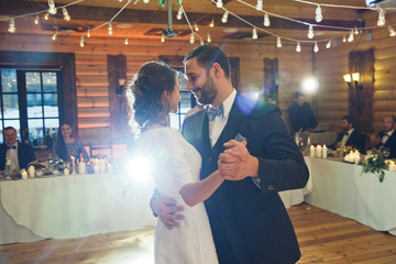 Stylish just married couple dances in the middle of wooden hall