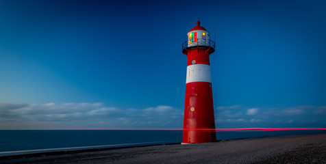 Red lighthouse during sunset on a dike at sea