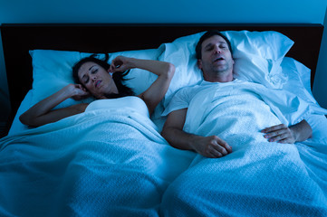 Fototapeta na wymiar Sleeping man with obstructive sleep apnea snoring loudly in bed while tortured wife plugs her ears
