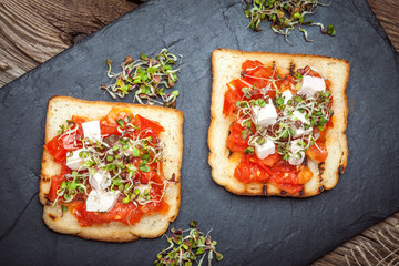 Grilled toasted bread with roasted tomatoes, feta cheese and radish sprouts.