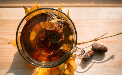 Autumn Still Life: Tea on maple leaves on a wooden table near the window. The sun's rays on a cup of brewed tea. Cup of hot tea on a sunny day on a window background.