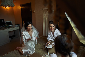 Fototapeta na wymiar The bride with bridesmaids drink a tea on the bed