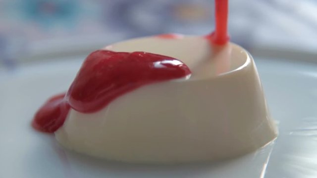 Slow motion close-up shot of pouring panna cotta dessert with strawberry sauce