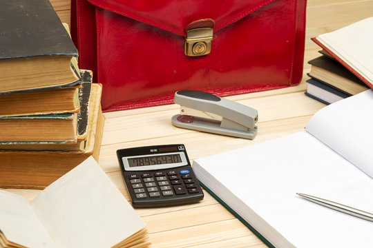 On A Wooden Table Books, Documents, Calculator, Red Briefcase.