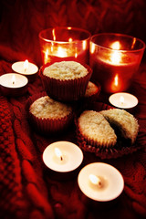 Soft focus. Muffins in a red wrapper on red knitted sweater, red candles and bokeh. Christmas atmosphere