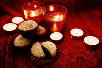 Soft focus. Muffins in a red wrapper on red knitted sweater, red candles and bokeh. Christmas atmosphere
