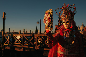 Plakat Lady in red costume looks at her mask in the big mirror standing