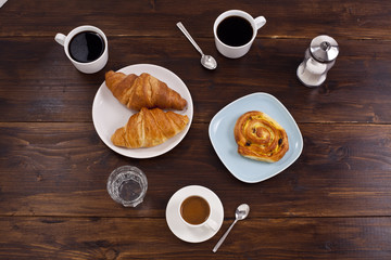 Coffee cups and croissant are on the wooden table.
