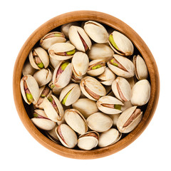 Roasted pistachio seeds with shell in wooden bowl on white background. Pistacia vera fruits and kernels. Isolated macro food photo close up from above.