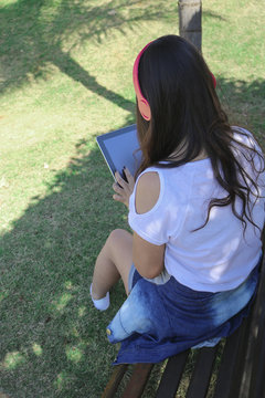 Beautiful young teenage girl wearing a set of headphones and using a smart phone in a park. Concept Image.
