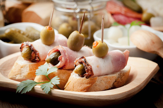 Tapas with sliced bacon, olives and cucumber on a wooden table.