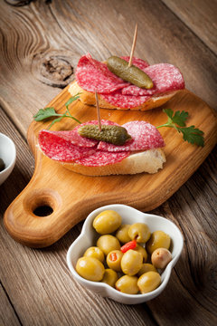 Tapas with sliced salami, olives and cucumber on a wooden table.