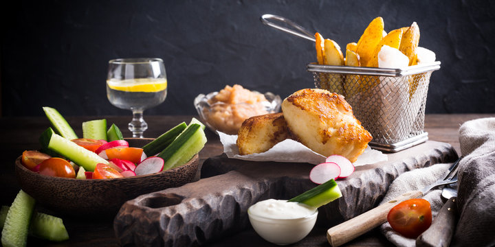 Fish and chips. Fried fish fillet with homemade baked potatoes and fresh salad on wooden cutting board.