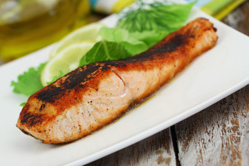 Grilled salmon steak with lemon and side salad on white plate
