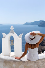 Frau mit weißem Kleid sitzt auf einer Mauer und schaut auf die Caldera von Santorini