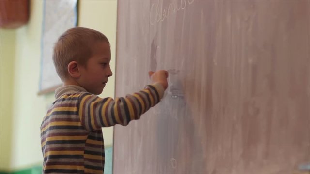 Boy writes on the blackboard at school/schooling, the boy writes chalk on blackboard