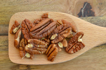 A spoon full of pecan halves on wooden background- healthy eating concept