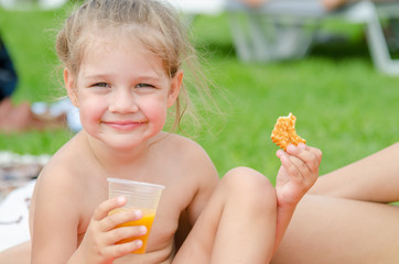 Girl eats cookies, drinks juice from a plastic disposable cup and smiling looked into the frame