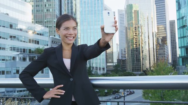 Business woman taking selfie photo using smart phone app on smartphone for social media. Young businesswoman using smartphone smiling happy wearing suit jacket outdoors. Urban female professional.