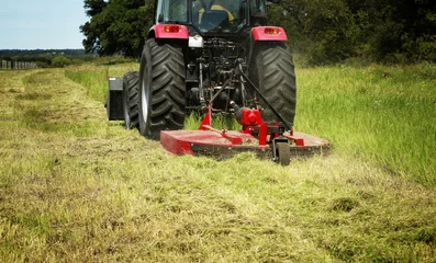Keuken spatwand met foto Farming: Large red tractor moving green farmers pasture, motion close up  © GalinaSt