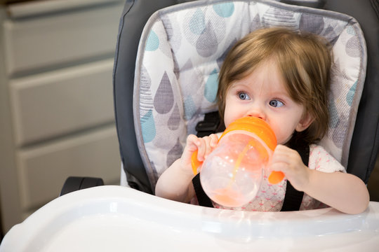 Portrait of baby girl drinking from bottle sitting in highchair