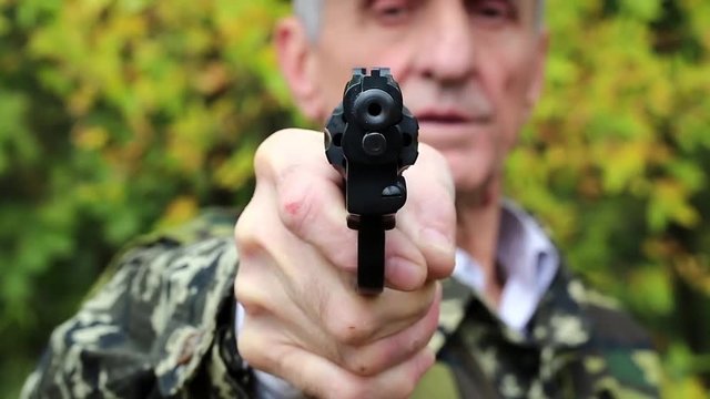 Man with black revolver in hand looks at the camera. Man with black gun. Retired officer in military uniform at shooting range. Man holds in hands black revolver