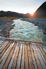 Landscape mountain river and a wooden bridge at sunset.