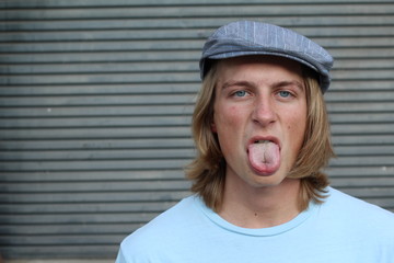 Closeup portrait, funny annoyed young childish rude bully man sticking his tongue out at you camera, isolated on gray background. Negative emotion facial expression feelings, signs, symbols