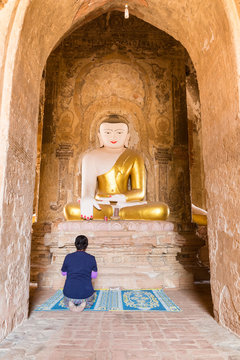 BAGAN, MYANMAR - FEB 20: Female traveller praying to ancient buddha statue in Shwe Laik Tu temple on February 20, 2016 in Bagan, Myanmar.