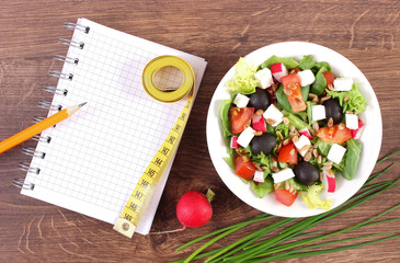Fresh greek salad with vegetables, centimeter and notepad for writing notes, healthy nutrition and slimming concept