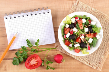 Fresh greek salad with vegetables and notepad for writing notes, healthy nutrition