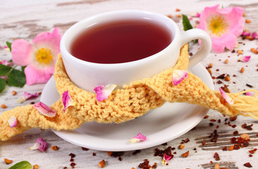 Cup of tea with wild rose flower on old rustic wooden background