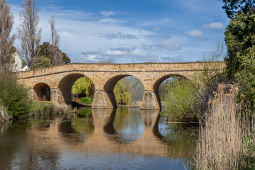 The iconic Richmond Bridge reflecting in water on bright sunny day. Richmond, Tasmania, Australia