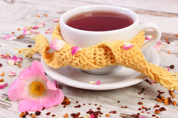Cup of tea with wild rose flower on old rustic wooden background