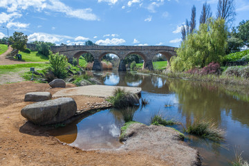 Fototapeta na wymiar The iconic Richmond Bridge reflecting in Coal river waters on bright sunny day. Richmond, Tasmania, Australia