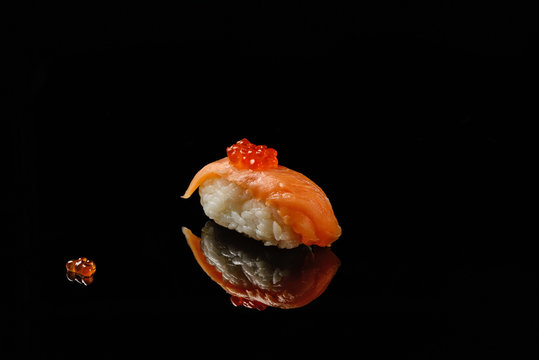 Sushi and red caviar on black acryle with reflection