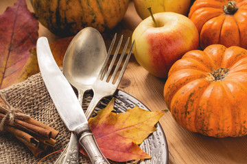 Autumn table setting for Thanksgiving day with pumpkins, apples, cinnamon sticks, fallen leaves and...