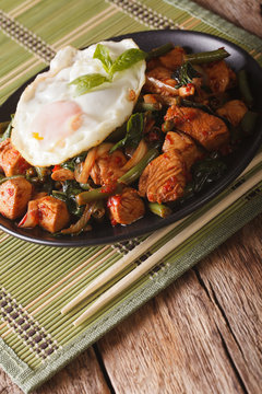 Thai cuisine chicken with basil, green beans and a fried egg close-up vertical
