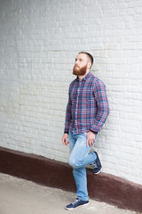 bearded man is leaning on a brick wall