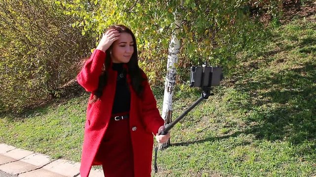 The girl in the red coat makes selfie with monopod
