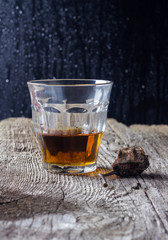 glass of whiskey with a dry pear on a wooden table with a black background in the drops