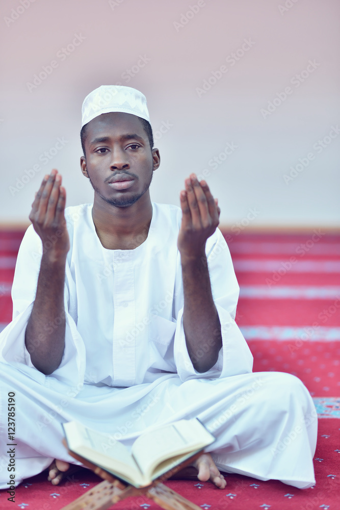 Wall mural African Muslim Man Making Traditional Prayer To God While Wearing A Traditional Cap Dishdash