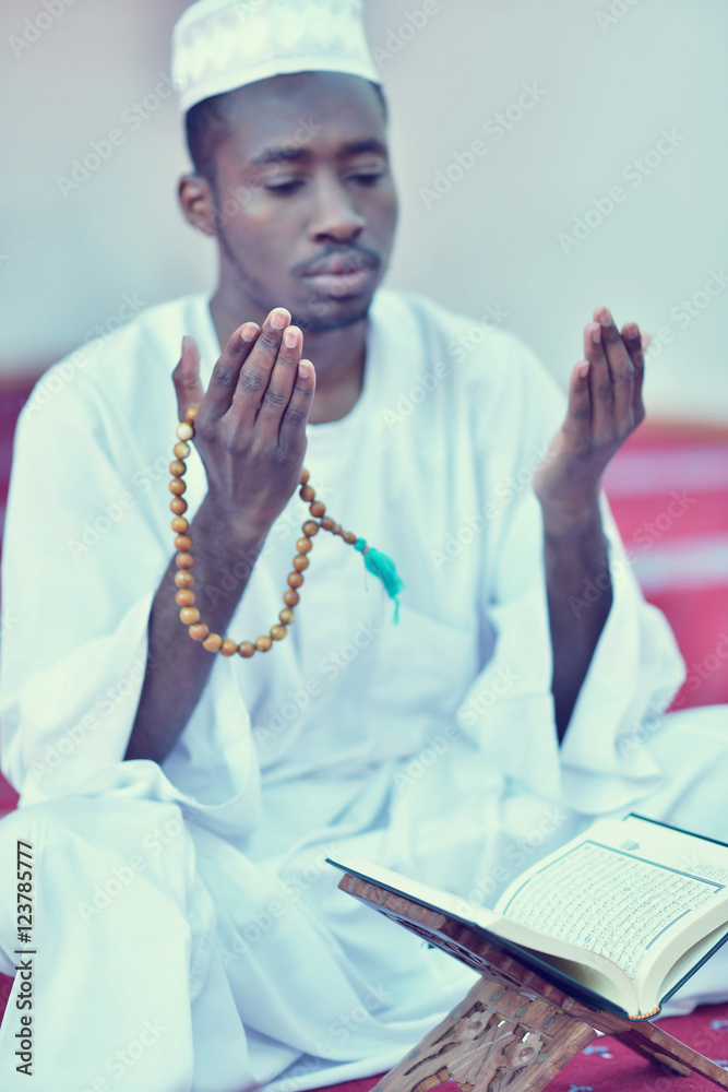 Wall mural African Muslim Man Making Traditional Prayer To God While Wearing A Traditional Cap Dishdash