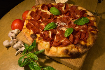 Pizza party fresh basil pepperoni tomatoes wooden cutting board on table