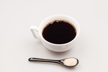 White coffee cup with coffee and black teaspoon with brown sugar