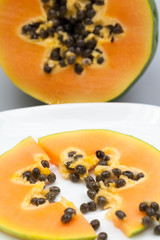 Papaya fruit - half and slice with seeds and light grey background