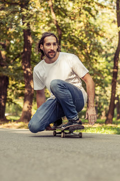 Skateboarder squatting on a skateboard and ride a slope on the road through the forest. Freeride skateboarding
