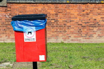 Red dog waste bin against a brick wall