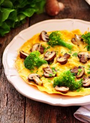 Scrambled eggs with mushrooms, broccoli, cheese and green onions on an old wooden table. Rustic style.