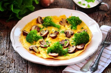 Scrambled eggs with mushrooms, broccoli, cheese and green onions on an old wooden table. Rustic style.
